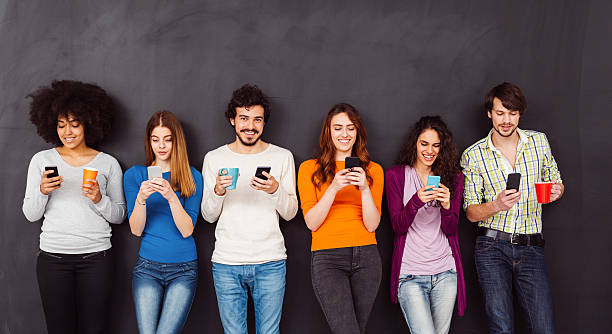 Young people text messaging Group of friends against blackboard using smartphones multi ethnic group college student group of people global communications stock pictures, royalty-free photos & images