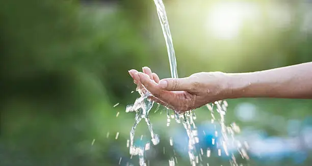 Photo of Water pouring in woman hand on nature background