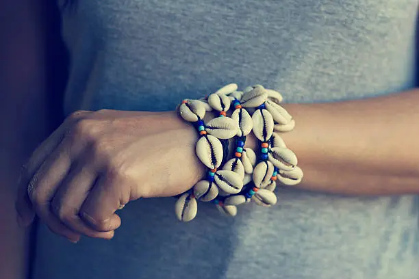 Cowrie shell bracelets on the wrist of woman, vintage color tone