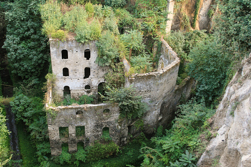 Ruins of the Abandoned Mill in the Vallone dei Mulini (Valley of the Mills) in Sorrento, Italy, green trees and steep cliffs are in the image.