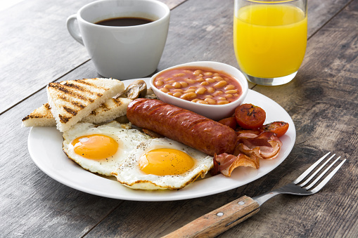 Traditional full English breakfast with fried eggs, sausages, beans, mushrooms, grilled tomatoes and bacon on wooden background