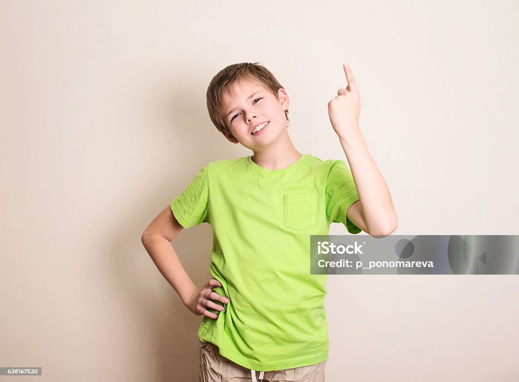 Cheerful teen boy pointing up over white background Cheerful teen boy pointing up over white wall. Boys Stock Photo