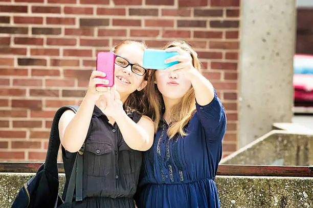 Photo of Teenage high school girls shooting selfies with mobile phones