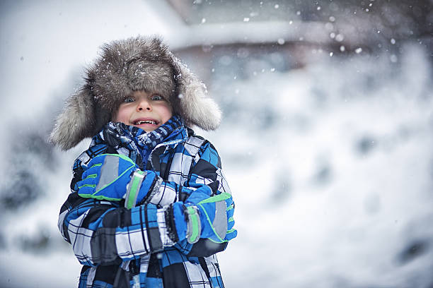 Winter portrait of little boy on a freezing day Portrait of a cute boy in big fake fur cap. It's snowing and freezing outside and the little boy is haking the winter day. Snow flakes are falling on the cap. shivering stock pictures, royalty-free photos & images