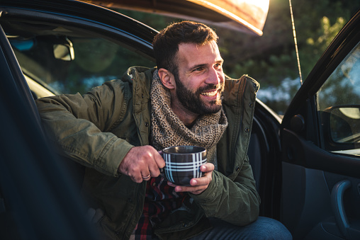 Handsome man drinking coffee while sitting in a car.