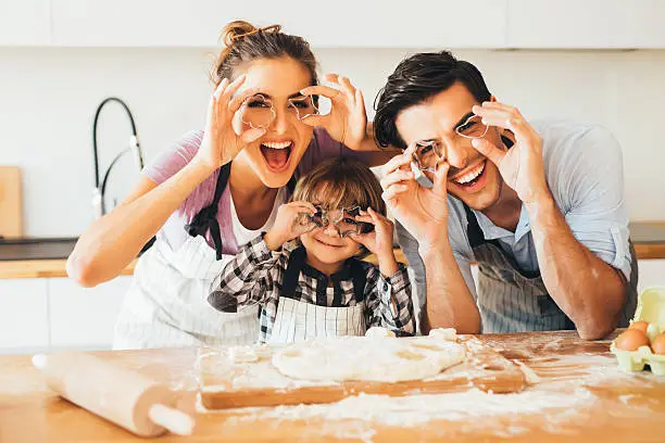 Young family holding cookie cutters in front of their eyes while making cookies in the kitchen.