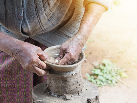 Old woman's hands sculpt clay pottery on wooden stand. The ancient production.