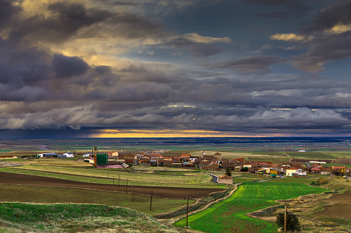 Dramatic stormy sky at sunset over the small village of Peñalba de Ávila, a village in Spain 17km from Madrid. Rain can be seen moving along the horizon, but sunlight lights up the sky.