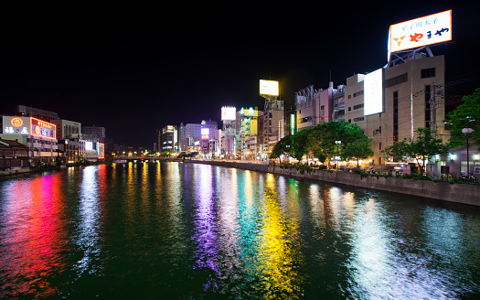 Still taken from time lapse video #542878824. Fukuoka riverfront district glowing in a dark night, making multicolored reflections on the water of the Naka River.