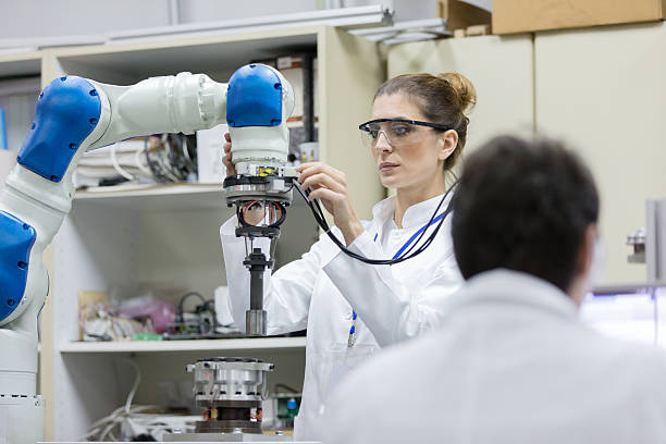 Engineers working in research lab Female engineers working in research lab, focus on woman in background using robotic arm robotic arm lab stock pictures, royalty-free photos & images