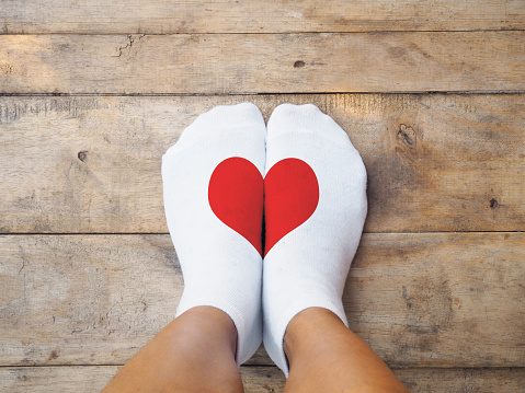Selfie feet wearing white socks with red heart shape on wooden floor background. Love concept.