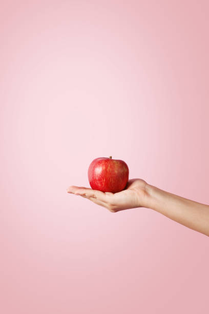 Woman hand holding a red apple on pastel background