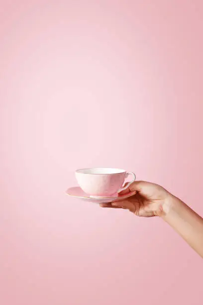 Woman hand holding a teacup on pastel background