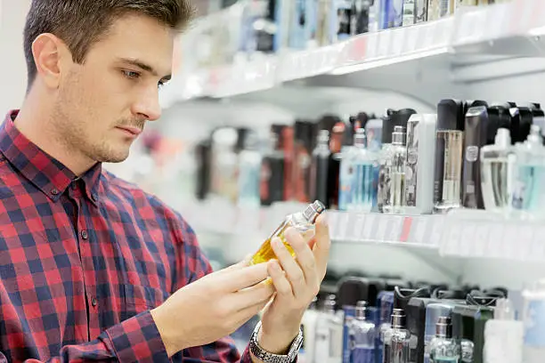 Man standing next to perfumes, holding perfume sample bottle