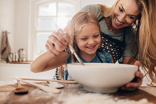 Young family cooking in kitchen Young family cooking food in kitchen. Happy young girl with her mother mixing batter in the bowl. jacob ammentorp lund stock pictures, royalty-free photos & images