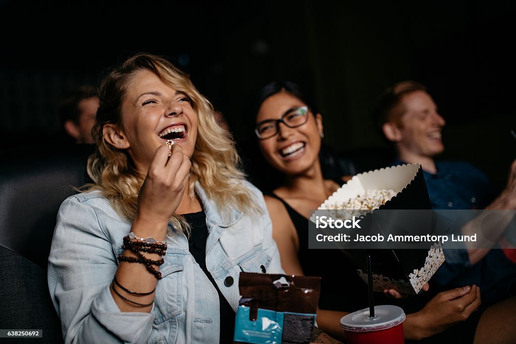 Young woman with friends watching movie Young woman with friends watching movie in cinema and laughing. Group of people in theater with popcorns and drinks. Movie Theater Stock Photo