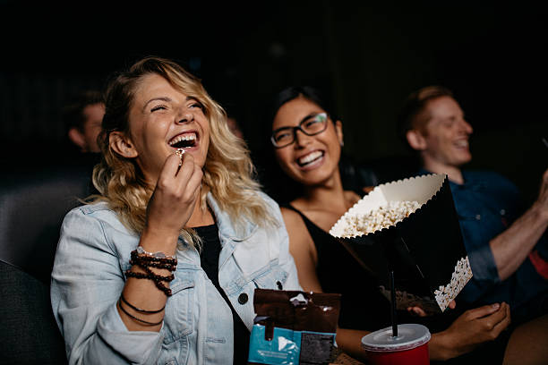 Young woman with friends watching movie Young woman with friends watching movie in cinema and laughing. Group of people in theater with popcorns and drinks. spectator stock pictures, royalty-free photos & images