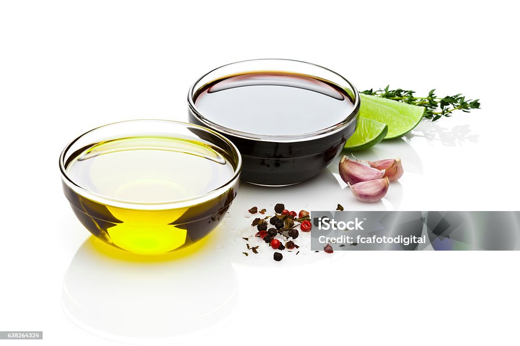 Olive oil and balsamic vinegar bowls on white backdrop Ingredients for a perfect vinaigrette, olive oil, balsamic vinegar, salt, pepper, garlic and lime isolated on reflective white background. DSRL studio photo taken with Canon EOS 5D Mk II and Canon EF 70-200mm f/2.8L IS II USM Telephoto Zoom Lens White Background Stock Photo