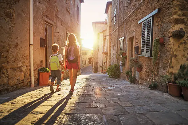 Photo of Brother and sister going to school in little town street.