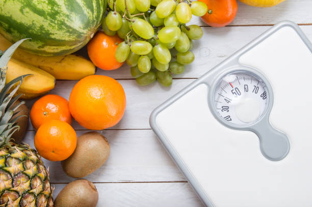 pila de frutas y báscula de peso blanco sobre tabla de madera. - weight scale apple comparison balance fotografías e imágenes de stock