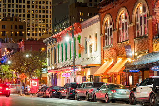 Photo of colorful bars, clubs and businesses at the famous Sixth Street music and entertainment district of downtown Austin, Texas, USA, illuminated at night.