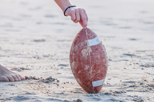 Close up of hand over from rugby ball on the beach. Hand of football player making touchdown. Sport concept and competition. Concept of summer vacation and leisure. Copy space.