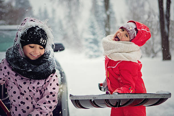 Two cute girls pulling his brother on a sled. Space for copy.