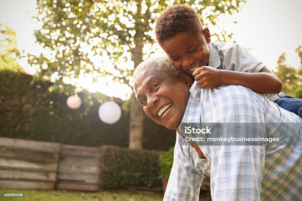 Joven negro subiendo a su abuelo de vuelta en el jardín - Foto de stock de Tercera edad libre de derechos