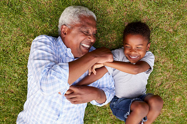 großvater und enkel spielen auf gras liegend, luftbild - großeltern stock-fotos und bilder