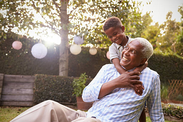 junge schwarze junge umarmt großvater sitzt im garten - grandson stock-fotos und bilder