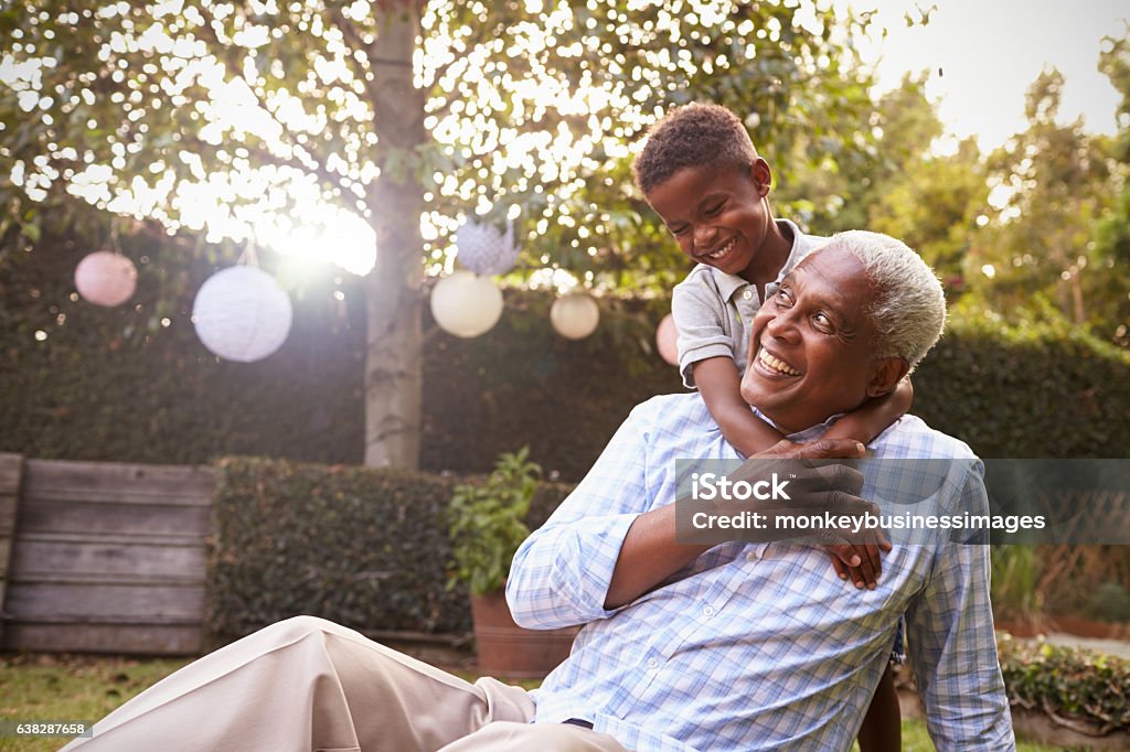 Jovem negro abraçando avô sentado no jardim - Foto de stock de Avô royalty-free