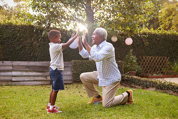 Black grandfather plays with grandson in garden, full length Black grandfather plays with grandson in garden, full length kneeling stock pictures, royalty-free photos & images