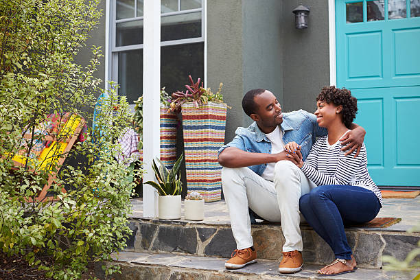 Young couple sit looking at each other outside their house