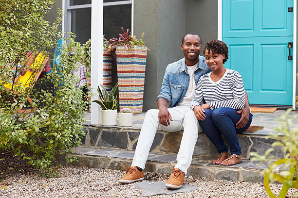 istock Young couple sit looking to camera outside their new house 638287880