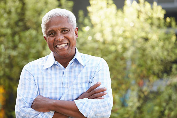 lächelnder afroamerikanischer mann mit gekreuzten armen - senioren männer stock-fotos und bilder
