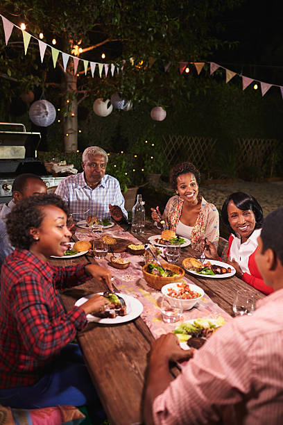 erwachsene schwarze familie genießen abendessen zusammen im garten, vertikal - face to face twilight togetherness vertical stock-fotos und bilder