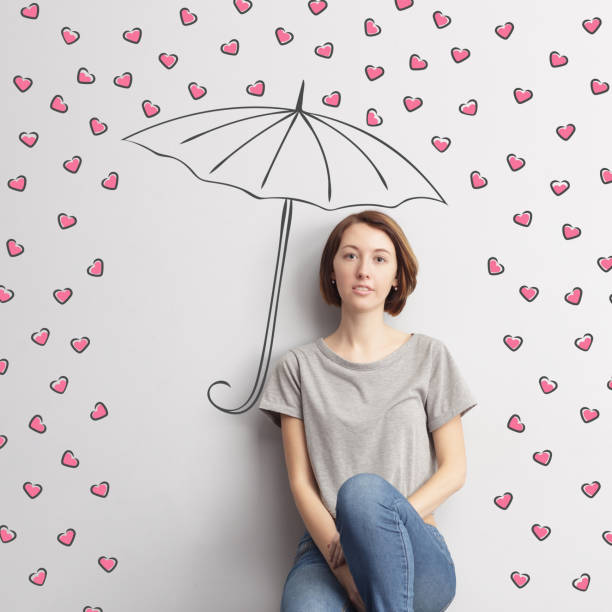 Beautiful girl sits under a painted umbrella, sheltering from the rain of hearts.