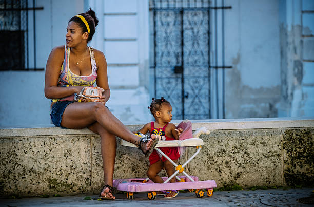 Havana, Cuba - October 13, 2016: Mother and child sitting on  the wall at the park on Prado Boulevard in Havana, Cuba. This is a famous downtown location, lined up with great architecture from past now mostly run down after years being exposed to elements from Caribbean sea. Popular place for people of Havana to hang around, be in love, play music and sport. A must see location when visiting this great city. Late afternoon in fall.