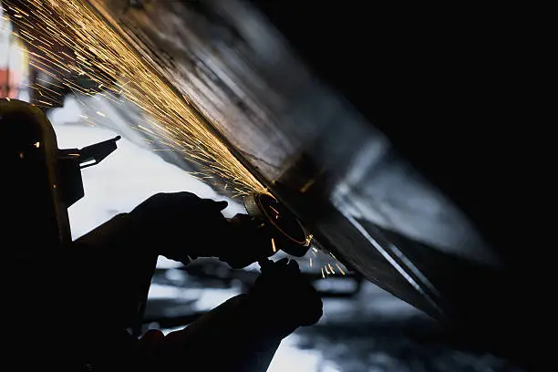 Welder working with grinder on side of a boat hull