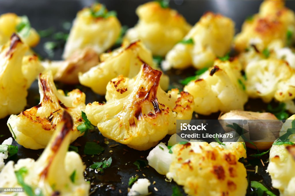 Oven baked spicy cauliflower with herbs and garlic. Oven baked spicy cauliflower on a black metal background. Cauliflower Stock Photo