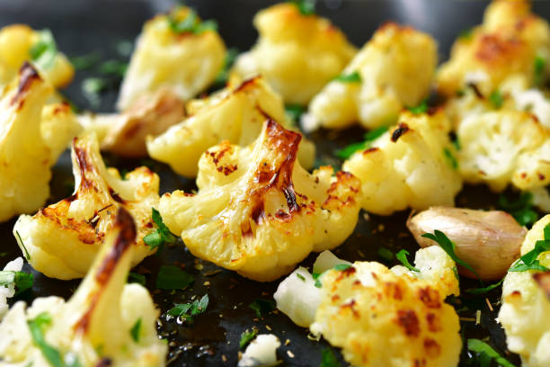 Oven baked spicy cauliflower with herbs and garlic. Oven baked spicy cauliflower on a black metal background. roasted stock pictures, royalty-free photos & images