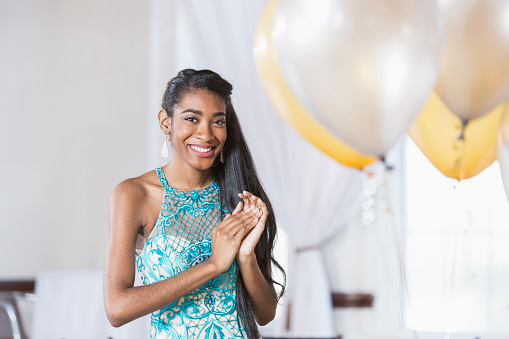 Portrait of an African American teenage girl wearing a formal dress, smiling at the camera. She is at a special event, perhaps a birthday party, or the prom.