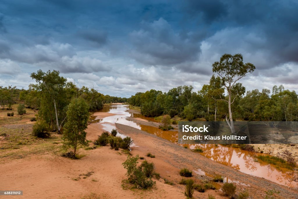 Finke River, Central Australia flowing after rain Finke River, South Australia, flows muddy and red after drought-breaking rain as it heads towards the western edge of the Simpson Desert. Outback Australian landscape off the Stuart Highway with dark storm clouds overhead. The source of the Finke River is in the MacDonnell Ranges in the Northern Territory. Finke River Stock Photo