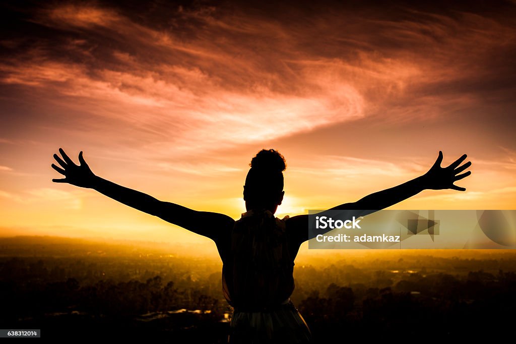 African American Woman Raising Arms at Sunset A young African American Woman raises her arms facing the sunset down over the valley and the ocean. Women Stock Photo