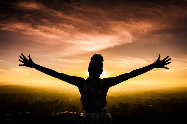 African American Woman Raising Arms at Sunset A young African American Woman raises her arms facing the sunset down over the valley and the ocean. african sunset stock pictures, royalty-free photos & images