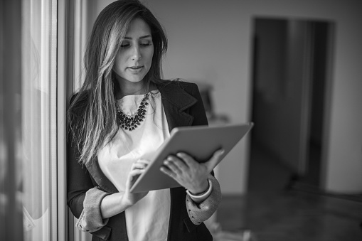 Young beautiful businesswoman standing next to the window and using digital tablet