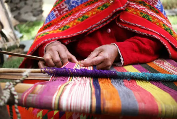 A close up of a woman weaving in Peru with bright traditional clothes.