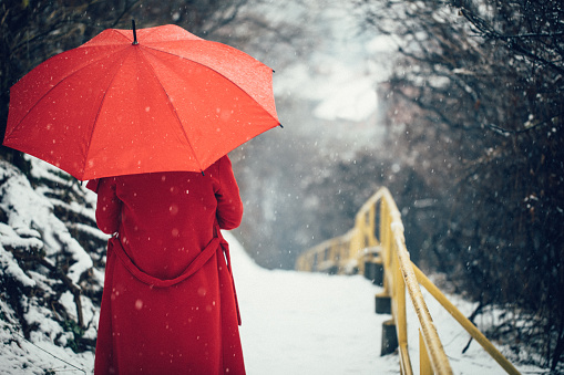 Woman in red coat with red umbrella enjoying the lovely first day of snow outdoors. Rear view.
