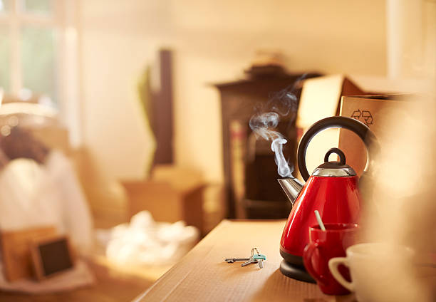 a steaming kettle sits next to some house keys amongst a pile of house move boxes .