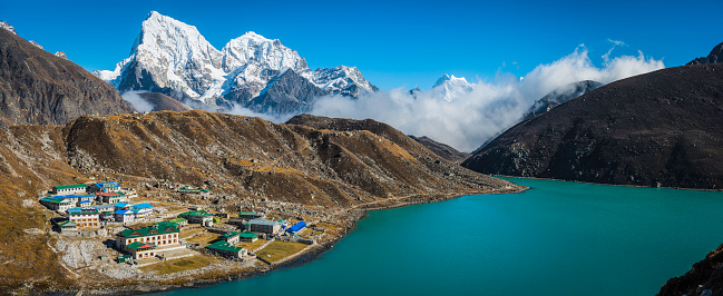 The snow capped summits of Tawoche (6542m) and Cholatse (6440m) overlooking the Sherpa village of Gokyo with its traditional teahouse lodges and blue glacial lake high in the Himalayan mountains of the Everest National Park, Nepal.